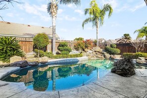 A backyard with a swimming pool, palm trees, and a wooden fence. - 3BR Family Home with Pool & Hot Tub (Fresno)
