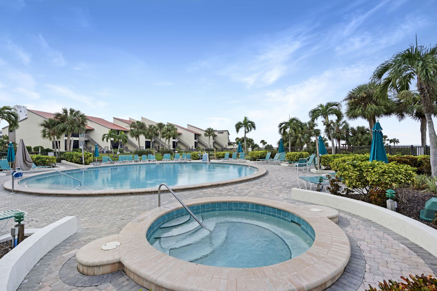 A pool area with a hot tub, lounge chairs, and palm trees.