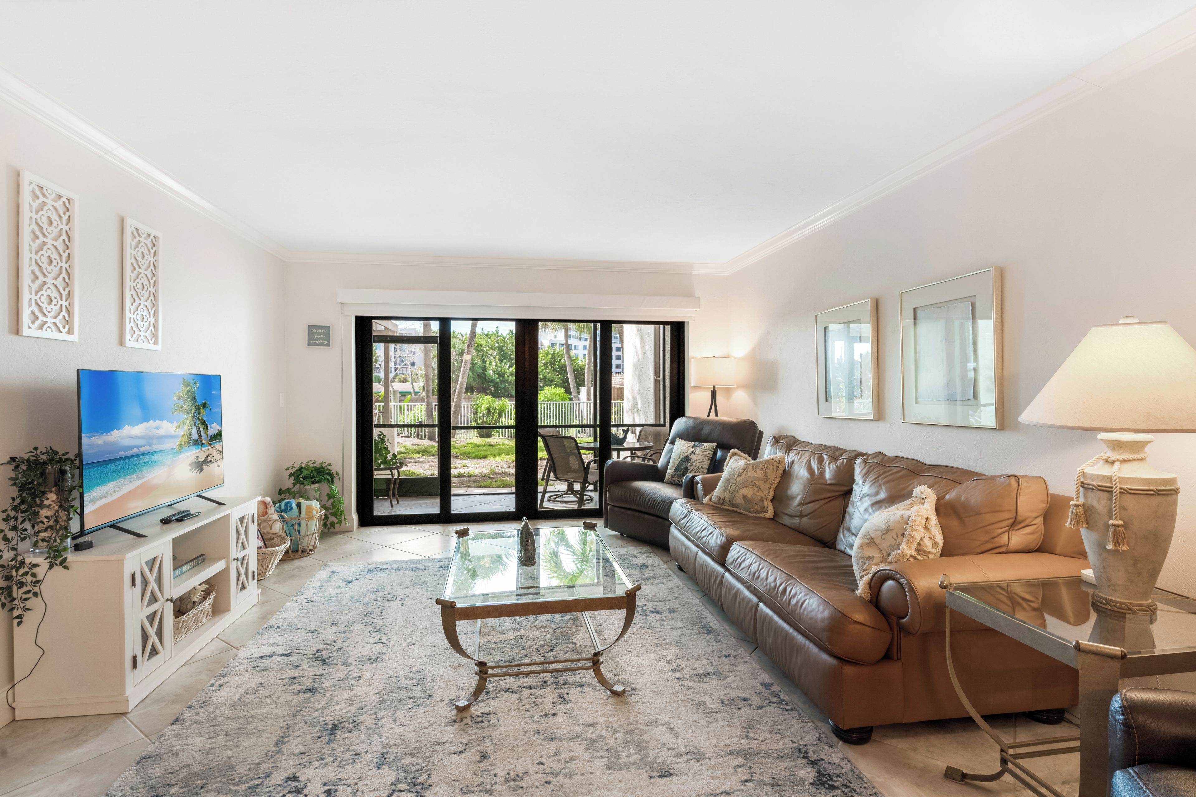 A living room with a sofa, coffee table, TV, and a view through a glass door to a garden.