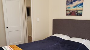 Een slaapkamer met een bed, een deur, een schilderij en een plafondlamp.