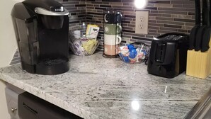 Een keuken met een koffiezetapparaat, waterkoker en broodrooster op het aanrecht. Ook staan er keukengerei en een afdruiprek.