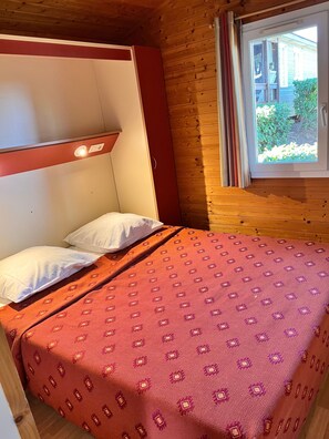 Una cama con colcha estampada, cabecera de madera y ventana con cortinas.