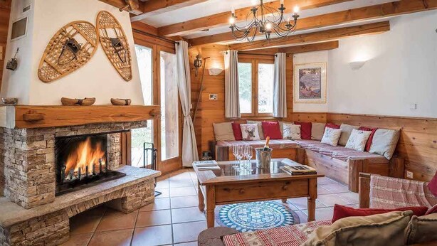 A cozy log cabin interior with a stone fireplace, wooden furniture, and a chandelier.