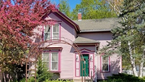 Une maison rose avec une porte verte, entourée d’un jardin et d’arbres.