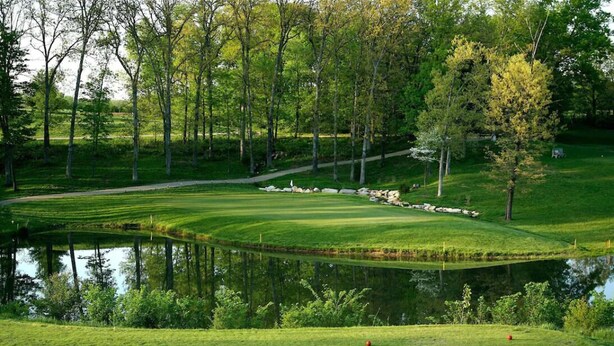Un parcours de golf agrémenté d’un étang, d’arbres et d’une pelouse bien entretenue.