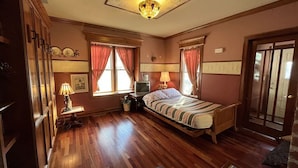 Une chambre avec un plancher en bois, un lit, un bureau avec une lampe et un téléviseur.