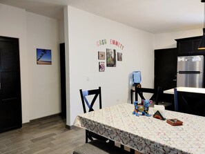 A dining area with a table covered by a floral tablecloth, chairs, a water dispenser, and a refrigerator.