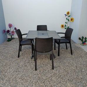 A square table with four chairs, surrounded by pebbles, with decorative flowers on the wall.