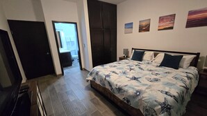 A bedroom with a bed, a wardrobe, a TV, and a bathroom visible through an open door.