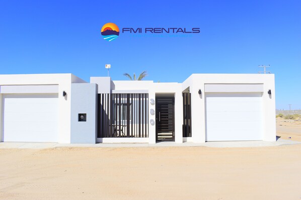 A modern building with a gated entrance, two garage doors, and a clear blue sky.