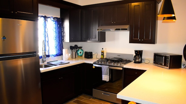 A modern kitchen with dark cabinets, stainless steel appliances, and a tiled backsplash.