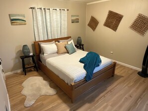 A bedroom with a wooden bed, white bedding, a white rug, and wall art.