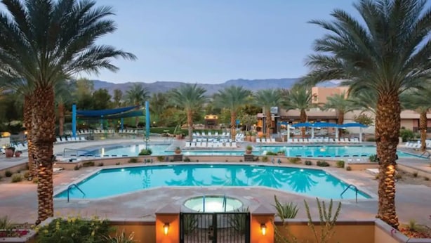 A resort pool area with multiple swimming pools, palm trees, and lounge chairs.