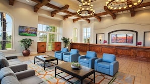 A spacious lobby with a wooden reception desk, blue seating area, and large windows offering views of the outdoors.
