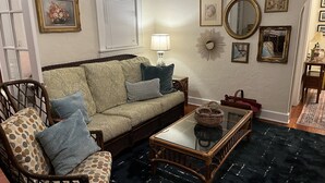 Een woonkamer met een bank, fauteuil en salontafel. Er zijn decoraties aan de muur, een lamp en een spiegel.