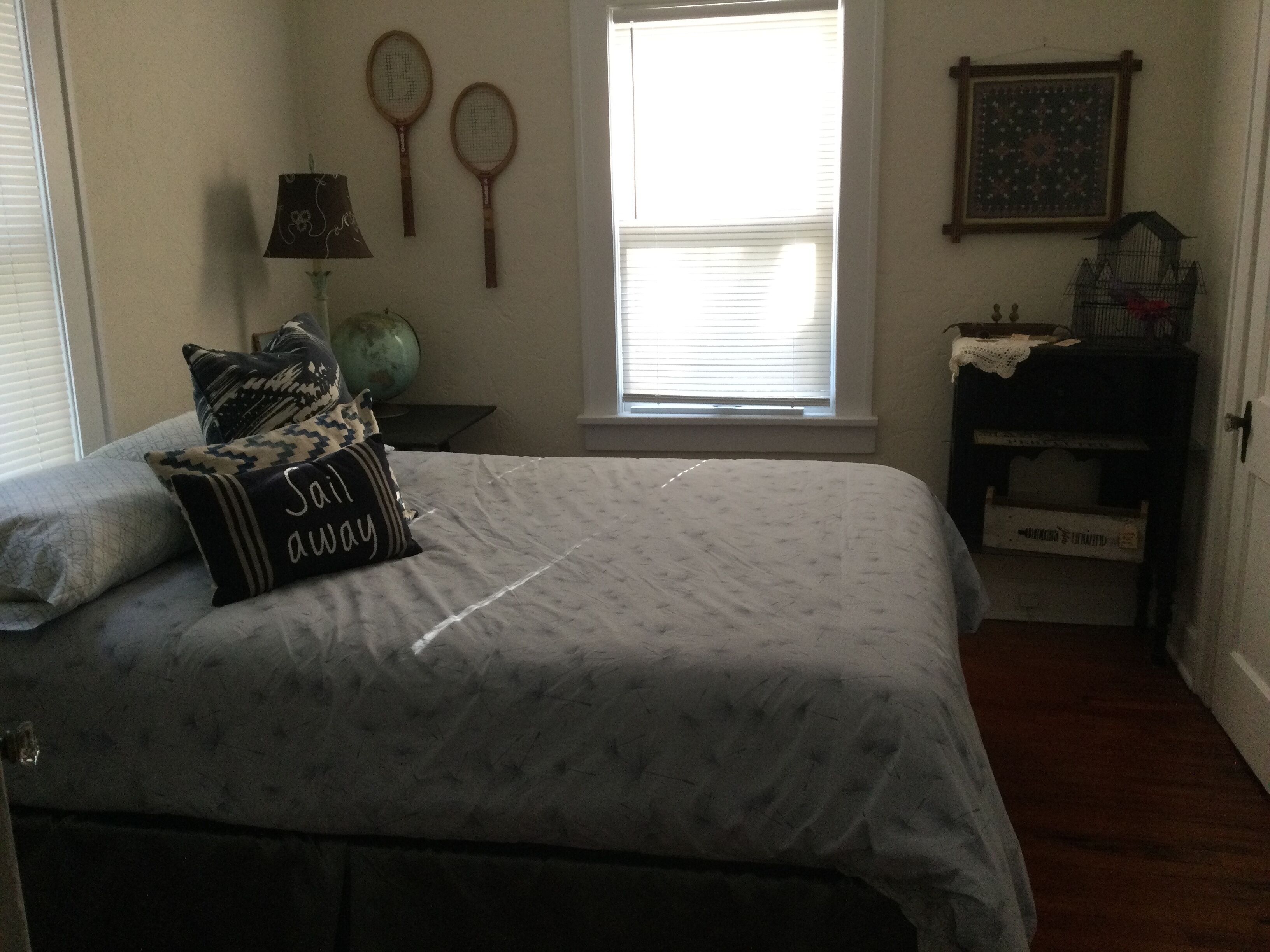 Ein Schlafzimmer mit einem Bett, Kissen, einem Fenster, einer Lampe und einem Bilderrahmen an der Wand.