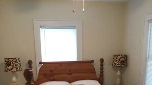 Een slaapkamer met een houten bed, twee nachtkastjes met lampen, een raam met jaloezieën en een vloerbedekking.