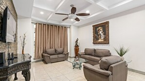 Ein modernes Wohnzimmer mit zwei Sofas, einem Glastisch, einem Deckenventilator und einem gerahmten Gemälde an der Wand.
