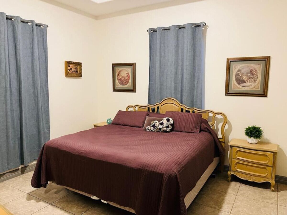 Un dormitorio con una cama grande, dos mesitas de noche y cortinas.