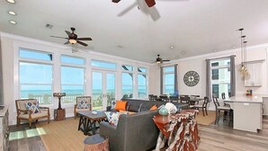 A spacious living area with a large window overlooking the ocean, a dining area, and a kitchen with a view. - Luxurious 6-Bedroom Oceanfront Home with Private Pool in Gulf County. (Port St. Joe)