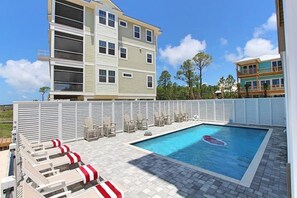A swimming pool with lounge chairs and a white fence.