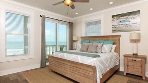 A bedroom with a wooden bed, a ceiling fan, a nightstand, and a view of the ocean through large windows. - Luxurious 6-Bedroom Oceanfront Home with Private Pool in Gulf County. (Port St. Joe)