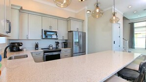 A modern kitchen with white cabinets, stainless steel appliances, and a large island with seating. - Luxurious 6-Bedroom Oceanfront Home with Private Pool in Gulf County. (Port St. Joe)