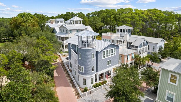 A large, multi-story house with a prominent tower and multiple balconies, surrounded by lush greenery.