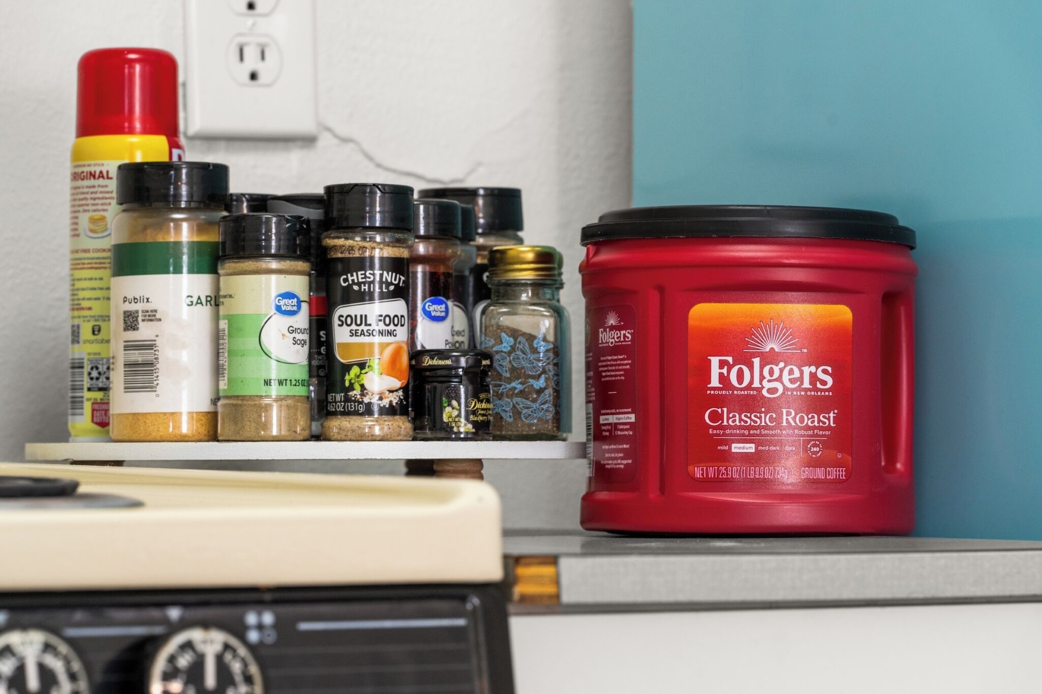 A kitchen counter with various spices and a container of Folgers Classic Roast coffee.