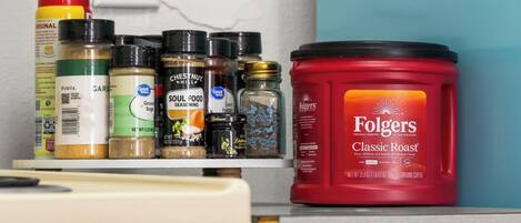 A kitchen counter with various spices and a container of Folgers Classic Roast coffee.
