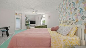 Ein Schlafzimmer mit einem Bett, einem Schreibtisch und einem Stuhl. Es gibt einen Deckenventilator und ein Fenster.