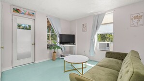 Ein Wohnzimmer mit einem grünen Sofa, einem runden Tisch, einem Fernseher auf einem Schrank und einer Tür mit satinierten Glasscheiben.