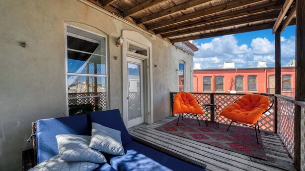 Ein Balkon mit einem blauen Sofa, zwei orangen Sesseln und einer Holzbalkendecke.
