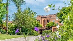 A building with a tiled roof, surrounded by lush greenery and flowering plants. - Amazing Ocean Views: Luxury Apartment @ Los Sueños (Playa Herradura)