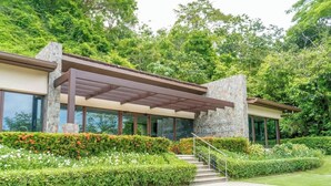 A modern building with a stone facade, large windows, and a covered entrance area. - Amazing Ocean Views: Luxury Apartment @ Los Sueños (Playa Herradura)