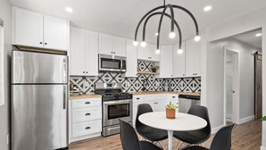 A modern kitchen with white cabinets, stainless steel appliances, a black and white patterned backsplash, and a round dining table with black chairs. - Mid Century Artsy Home in the Heart of NORTH PARK (San Diego)