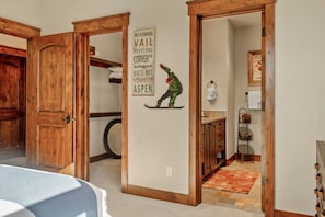A hallway with wooden doors, a wall-mounted sign listing locations, a small shelf with a decorative item, and a patterned rug. - Gorgeous Summit County Family Oasis (Silverthorne)