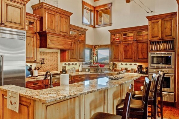 A spacious kitchen with wooden cabinets, a large island, stainless steel appliances, and a view of the mountains. - Gorgeous Summit County Family Oasis (Silverthorne)