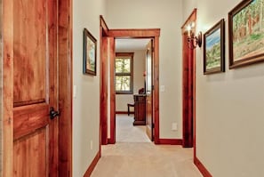A hallway with wooden doors and walls, framed artwork, and a window with natural light. - Gorgeous Summit County Family Oasis (Silverthorne)