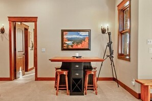 Una habitación con un escritorio de madera, dos taburetes, un telescopio y un cuadro de un paisaje colgado en la pared.