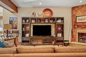 A living room with a large flat-screen TV, wooden entertainment center, and a stone fireplace.