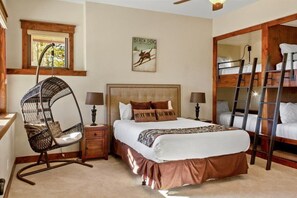 Un dormitorio con una cama grande, un sillón colgante, una escalera y una ventana con vistas a árboles.
