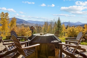 An outdoor seating area with Adirondack chairs and a grill, overlooking a mountainous landscape.