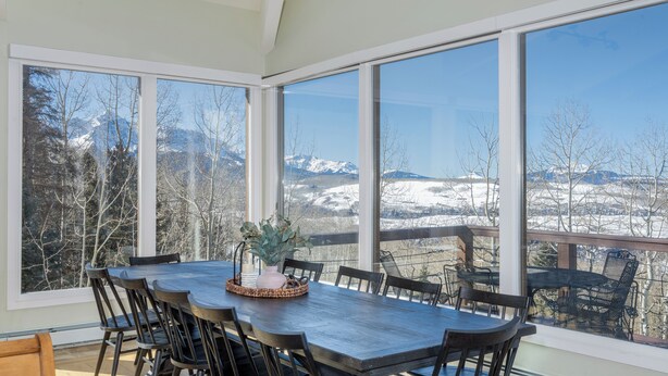 Ein Essbereich mit großem Tisch und Stühlen, große Fenster mit Blick auf die Berge.