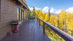 Eine Holzterrasse mit einem Grill, mit Blick auf einen Wald mit Herbstlaub und entfernte Berge.