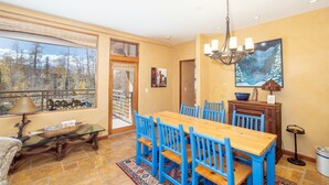 A dining area with a wooden table and blue chairs, a chandelier, and a painting on the wall. - Gorgeous Granita Ski in/Ski out (Telluride)