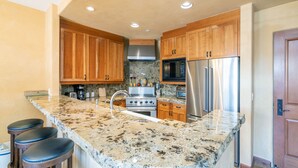 A kitchen with wooden cabinets, stainless steel appliances, granite countertops, and bar stools. - Gorgeous Granita Ski in/Ski out (Telluride)