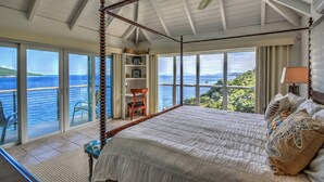 Ein Himmelbett mit Blick auf das Meer, ein Deckenventilator und ein Bücherregal.