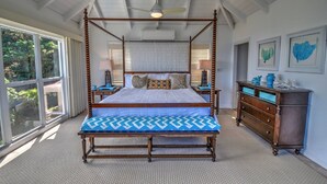Ein Bett mit Baldachin, dessen Himmel mit einem blauen und weißen Muster versehen ist, eine Holzbank am Fußende, ein Nachttisch mit Lampe sowie eine Kommode mit dekorativen Gegenständen.