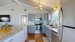 Une cuisine moderne avec des meubles gris, des appareils en acier inoxydable, un plancher en bois et une grande fenêtre équipée de stores.